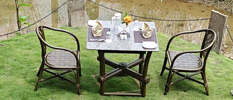 A picnic setup with a table and two chairs on a grassy area near a pond.