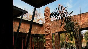 A courtyard with a large stone sculpture, a brick building, and a covered area with a metal roof. - Tathastu Bandhavgarh (Manpur)