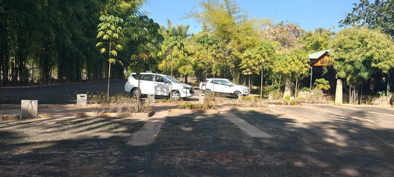 A parking area with two white cars parked, surrounded by trees and a small building with a sloped roof.