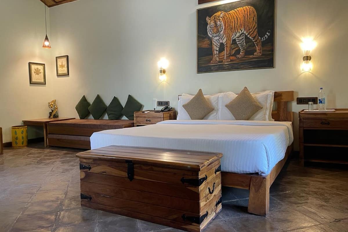 A spacious bedroom with a large bed, wooden headboard, and a wooden chest of drawers. There are wall-mounted lights and a tiger painting above the bed.
