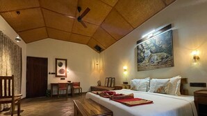 A spacious room with a large bed, wooden headboard, a ceiling fan, and a painting of a tiger. - Tathastu Bandhavgarh (Manpur)