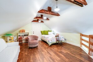 Un dormitorio de buhardilla acogedor con techo inclinado, vigas de madera, una cama con colcha colorida, una silla y un escritorio con lámpara.