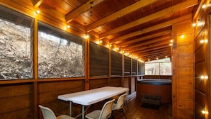 Une cabane en bois avec une table et des chaises, de grandes fenêtres et un jacuzzi.