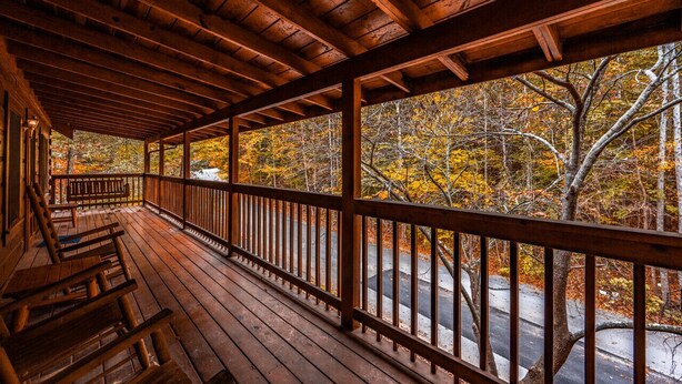 Une véranda en bois avec des bancs, une balustrade et une vue sur les arbres aux couleurs automnales.