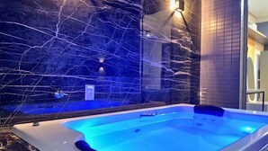 Un baño moderno con pared de mármol, cabina de ducha de cristal y bañera de hidromasaje integrada.