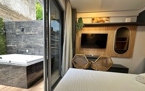 Une chambre moderne dotée d’une porte coulissante en verre, d’un téléviseur encastré, d’un meuble TV en bois, d’un petit coin salon avec deux fauteuils et d’une grande fenêtre.
