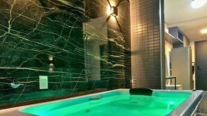 Un área de spa con una bañera de hidromasaje iluminada en verde, paredes de mármol y un diseño moderno.