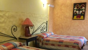 A room with two beds, each with a colorful quilt, a small table with a lamp, and a painting on the wall. - Hotel Mezvall (Morelia)