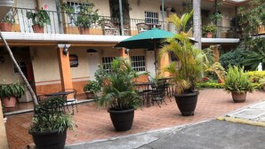 A courtyard with potted plants, outdoor seating, and a building with balconies. - Hotel Mezvall (Morelia)