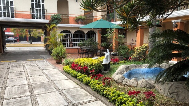A courtyard with a stone pathway, outdoor seating, and a statue. - Hotel Mezvall (Morelia)