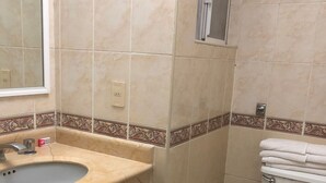 A bathroom with a beige sink, a mirror, a toilet, and a trash bin. - Hotel Mezvall (Morelia)