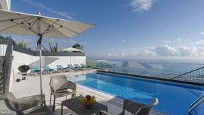 Un espace piscine aménagé sur le toit, avec des chaises longues, une table garnie de fruits et une vue sur un pont et le paysage urbain.