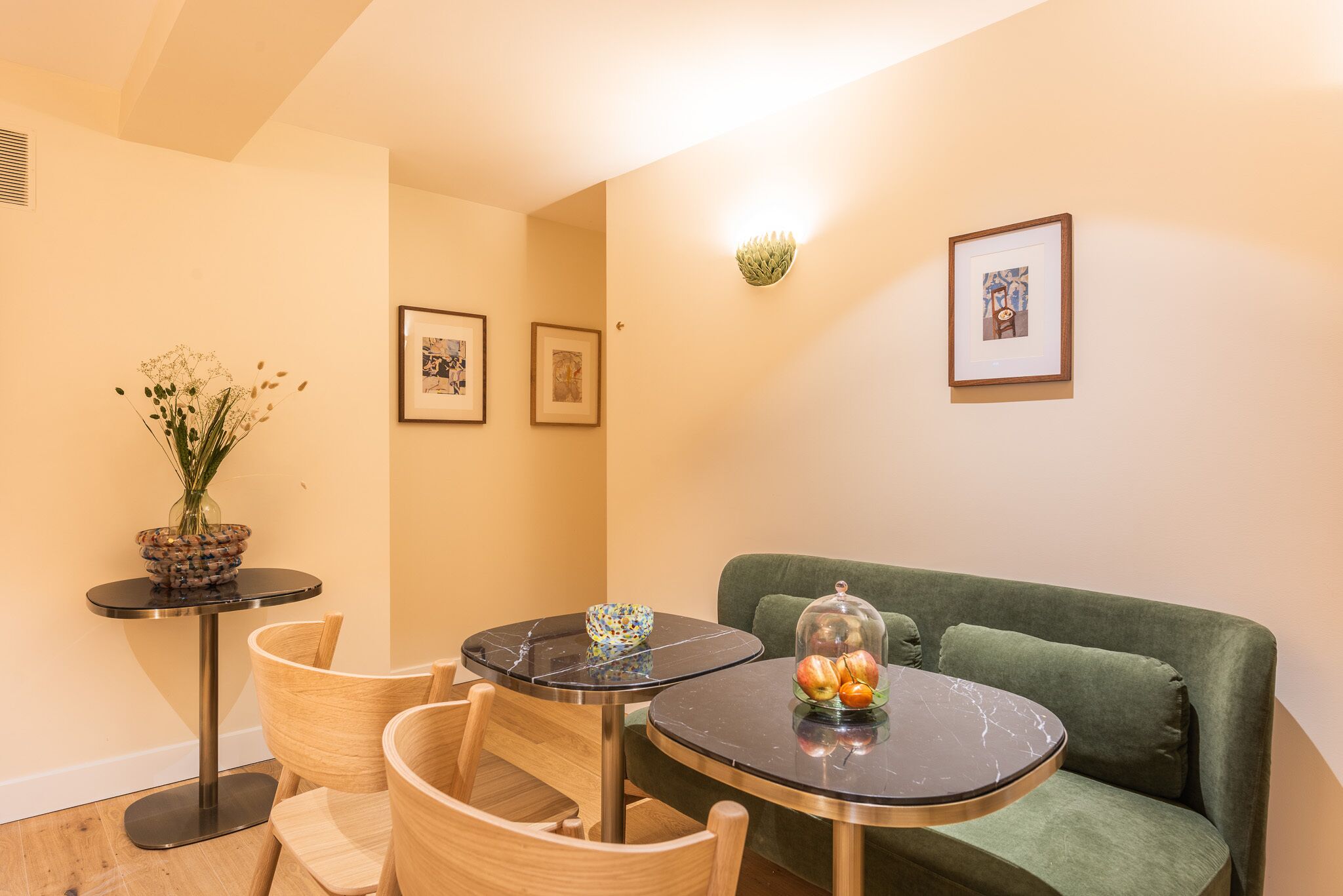 Una habitación acogedora con un sofá verde, una mesita redonda con una cúpula de vidrio y un jarrón con flores.
