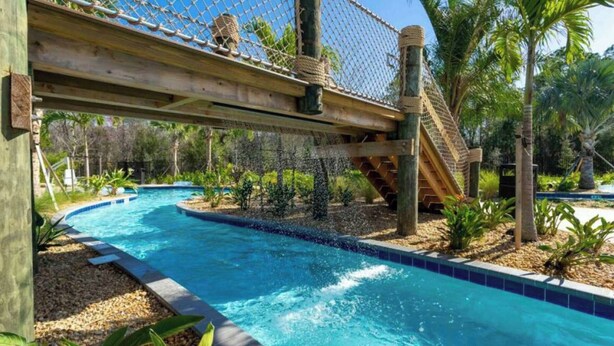 Zona de piscina con un puente de madera y una estructura de escalada con cuerdas.