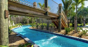 A pool area with a wooden bridge and rope climbing structure.