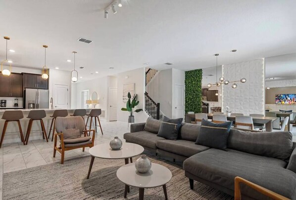 A modern living room with a grey sofa, two round coffee tables, and a dining area with chairs.