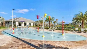 Un parque acuático con piscina, chorros de agua y sillas de descanso.