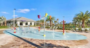 Um parque aquático com piscina, jatos de água e cadeiras de descanso.