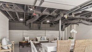 Un interior moderno con conductos expuestos, una mesa blanca, sillas de mimbre y un sofá.