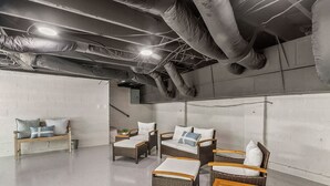 Habitación con mobiliario de mimbre, que incluye un sofá, sillas y una pequeña mesa. Se observan tuberías y una lámpara en el techo.