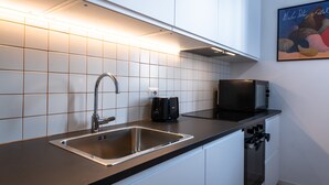 Et moderne køkken med stålvask, sorte hårde hvide skabe og et flisebeklædt bagvæg.