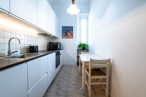 Una cocina estrecha con armarios blancos, encimera negra, un lavabo, una estufa y una mesa de comedor con sillas.