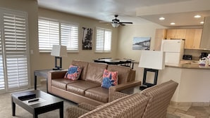 Una sala de estar con un sofá marrón, sillones estampados, una mesa de centro y una zona de comedor con mesa y sillas.