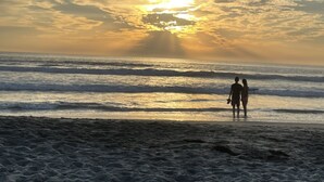 Una playa con un atardecer, olas y una persona caminando.