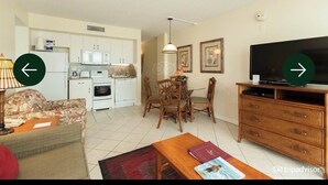 A living room with a sofa, coffee table, and a television. There is a dining area with a table and chairs. The kitchen is visible in the background. - Luxury Coastal Escape Beachfront Daytona Bike Week (Ormond Beach)