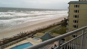 A view of a beach with a pool and lounge chairs, a building with balconies, and a cloudy sky. - Luxury Coastal Escape Beachfront Daytona Bike Week (Ormond Beach)