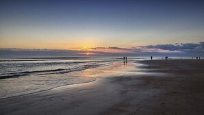 A beach with a sunset, calm waves, and people walking along the shore. - Luxury Coastal Escape Beachfront Daytona Bike Week (Ormond Beach)