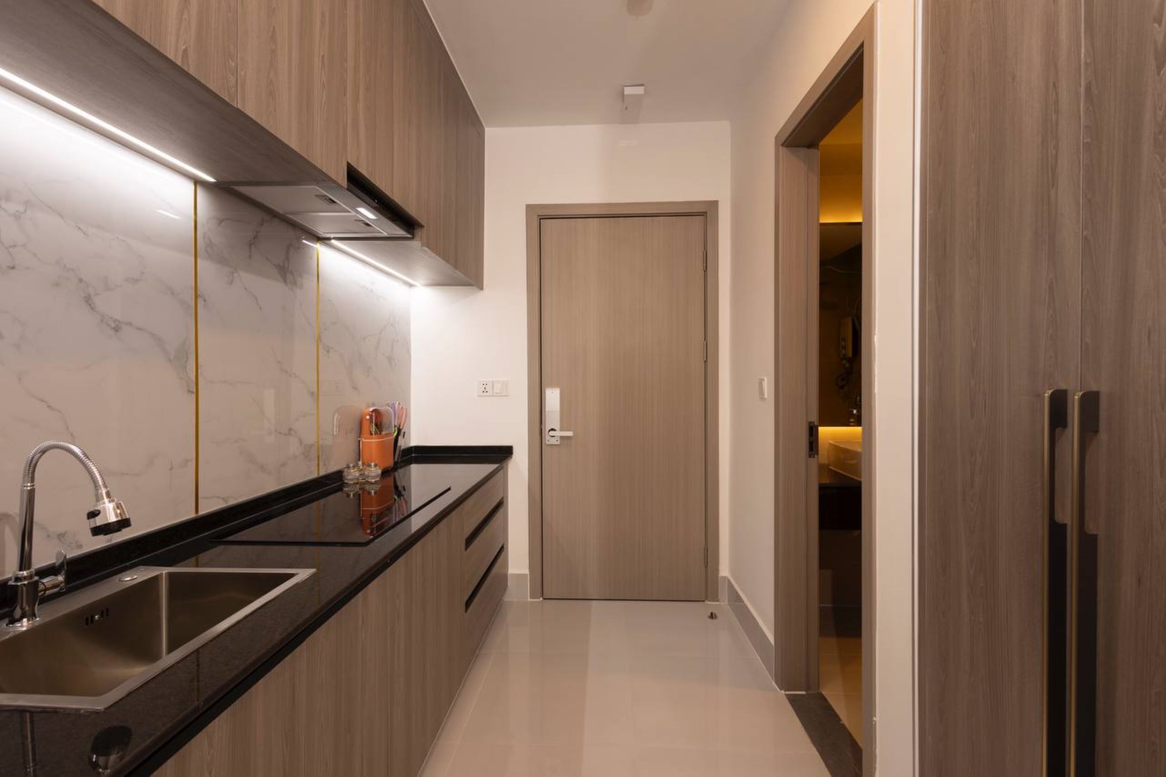 A modern kitchen with a marble countertop, stainless steel sink, and wooden cabinets.