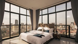 A spacious bedroom with a large bed, a nightstand, and a view of the city through floor-to-ceiling windows. - La Cozii TK (Phnom Penh)
