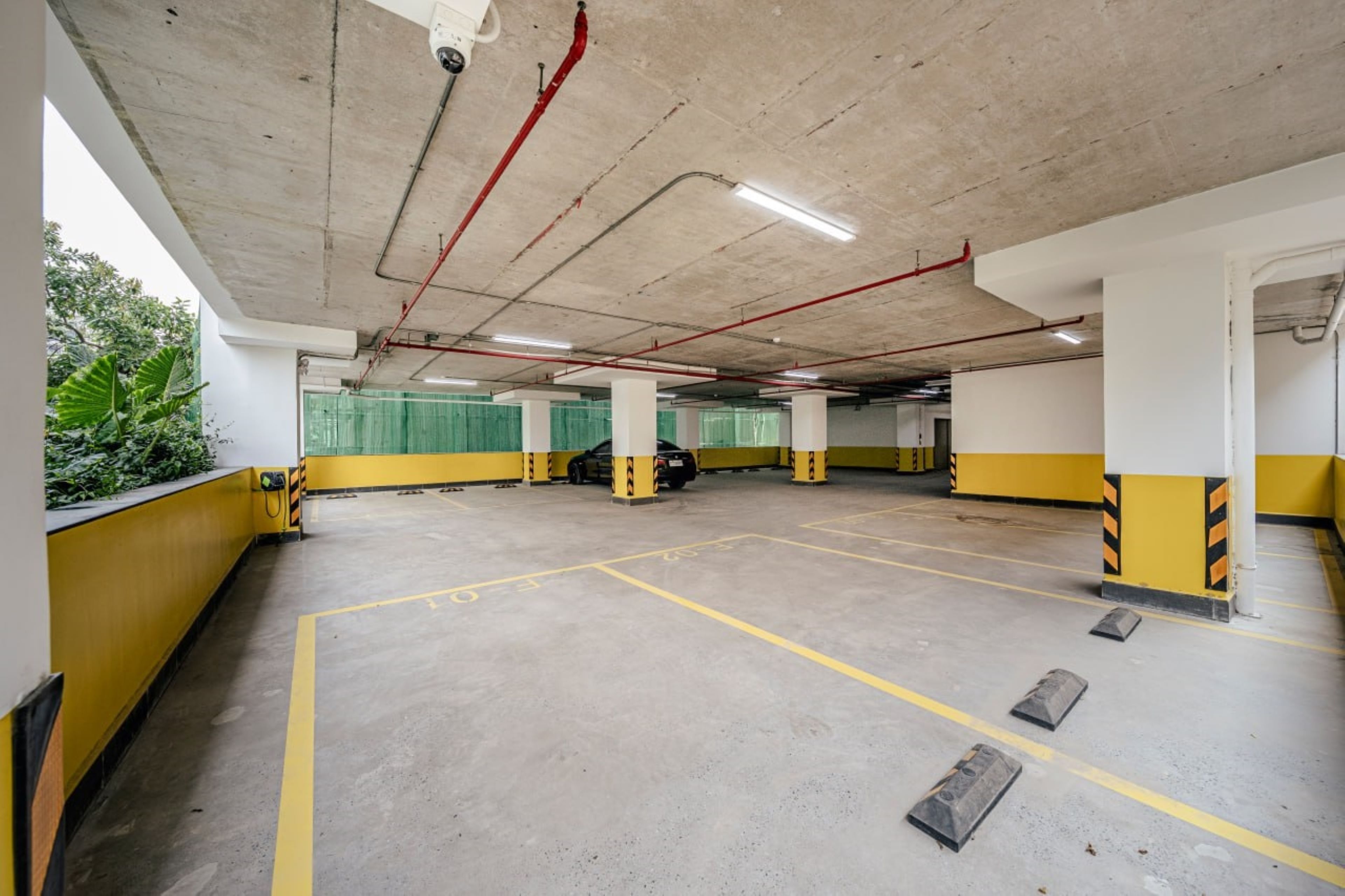 An empty parking garage with yellow and white walls, concrete floors, and visible structural elements like pipes and columns.