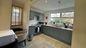 A kitchen with grey cabinets, a window with a view of greenery, a sink, and a small trash bin. - Stay at the Granary Villa, your home from home. (Shenstone)