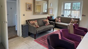 A living room with a striped sofa, a cushioned armchair, a red rug, and a large mirror. - Stay at the Granary Villa, your home from home. (Shenstone)