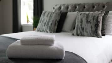 A neatly made bed with white linens and two folded towels on a dark ottoman.