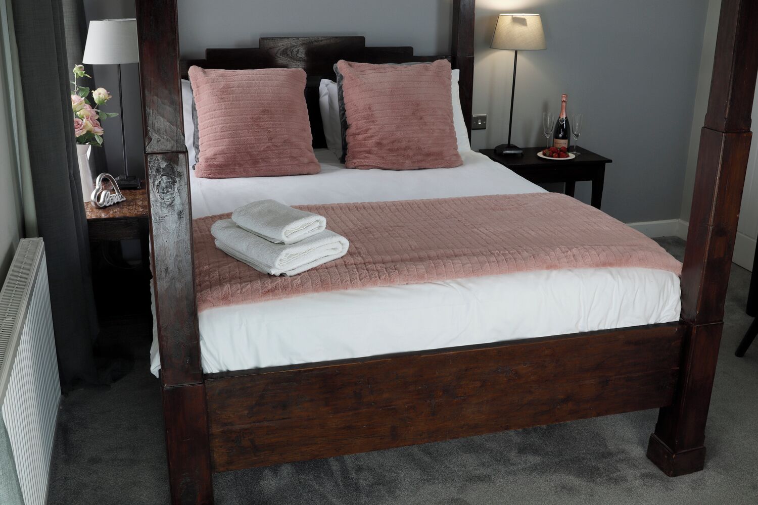 Una cama con dosel con una colcha blanca y rosa, dos almohadas rosas y toallas blancas dobladas al lado.