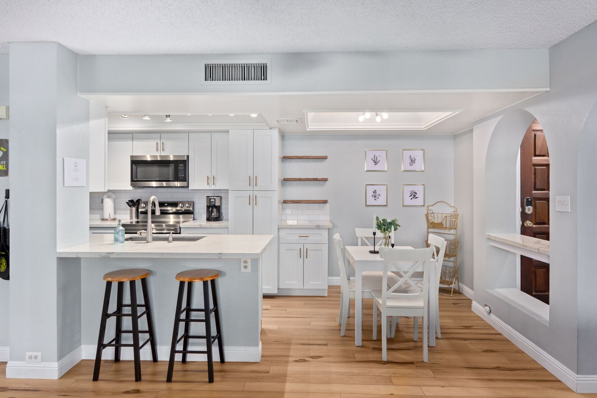 A modern kitchen with white cabinetry, a central island with stools, and a dining area with white chairs.