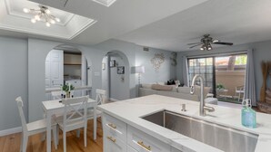 A modern kitchen with a central island, a dining area with white chairs, and a ceiling fan. - Pickleball, Pools, Internet, Free Parking, Paradise (Phoenix)