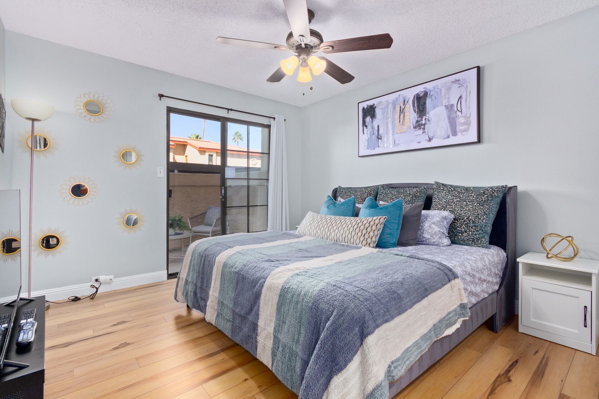 A bedroom with a bed, a ceiling fan, a window, and a painting on the wall.