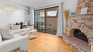 A modern living room with a stone fireplace, a sofa, a coffee table, and a glass door leading to a balcony. - Pickleball, Pools, Internet, Free Parking, Paradise (Phoenix)
