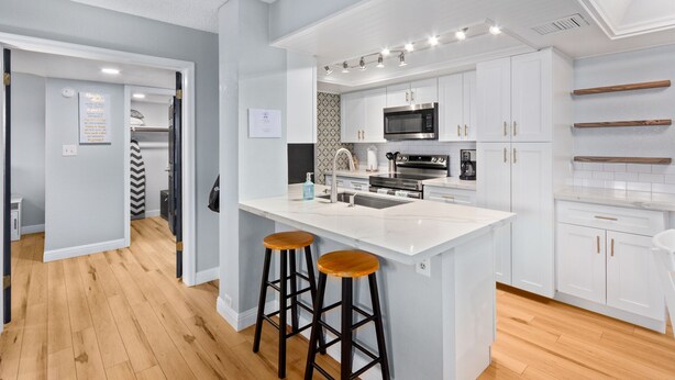 A modern kitchen with white cabinetry, a central island with stools, stainless steel appliances, and a patterned backsplash. - Pickleball, Pools, Internet, Free Parking, Paradise (Phoenix)