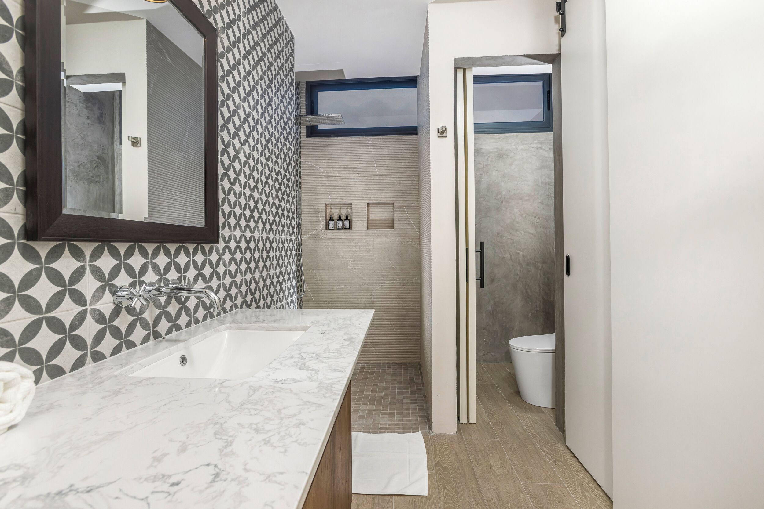 Une salle de bain moderne avec un lavabo en marbre, un grand miroir, des carreaux muraux à motifs, un espace douche et des toilettes.