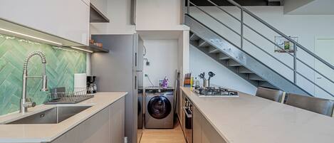 A modern kitchen with a built-in washer and dryer, a stainless steel sink, and a staircase leading to an upper level.