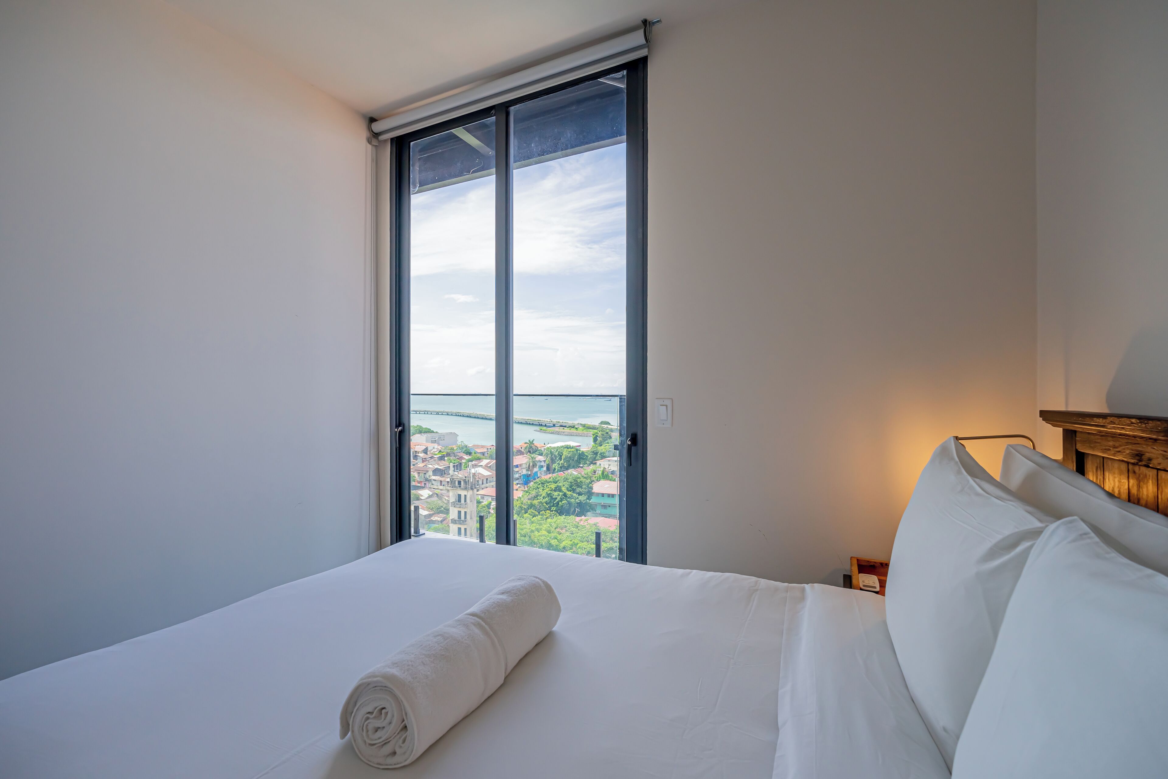 A hotel room with a large window offering a view of a cityscape and a body of water.