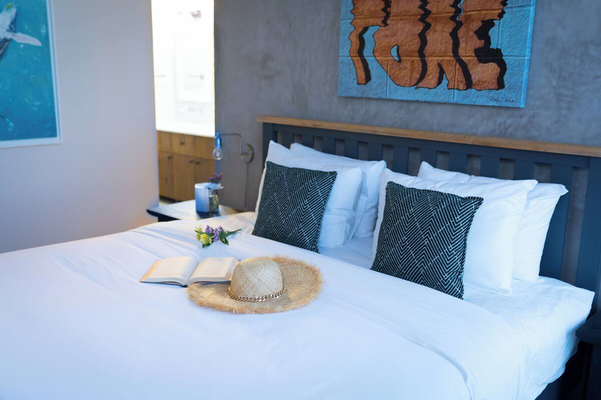A neatly made bed with a straw hat, pillows, and a book on a white bedspread.