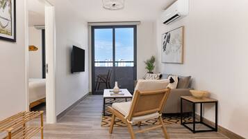 A modern living room with a sofa, a wicker chair, a small table, and a TV mounted on the wall.