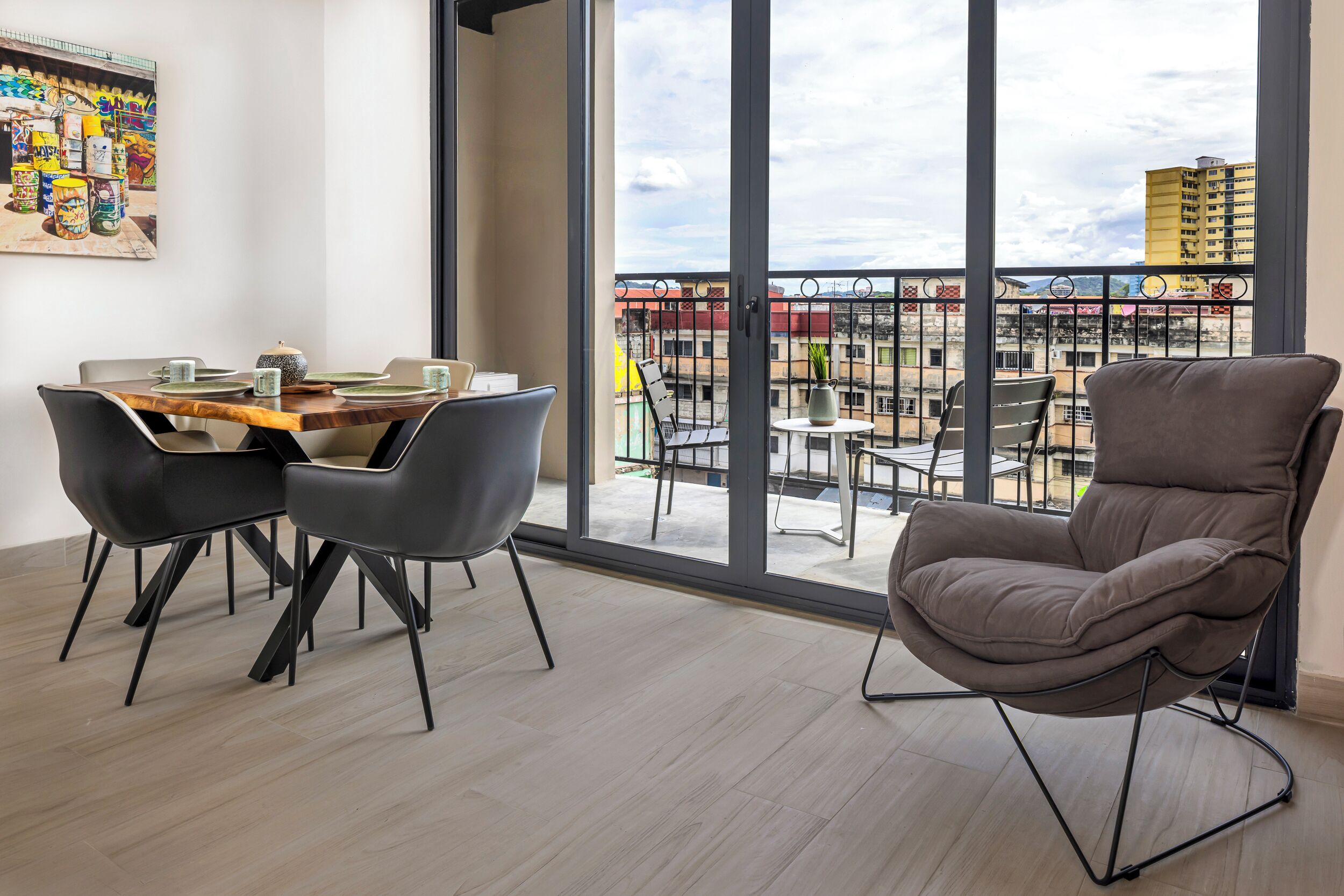 Una habitación moderna con balcón, una mesa de comedor con sillas y un amplio ventanal con vistas a la ciudad.