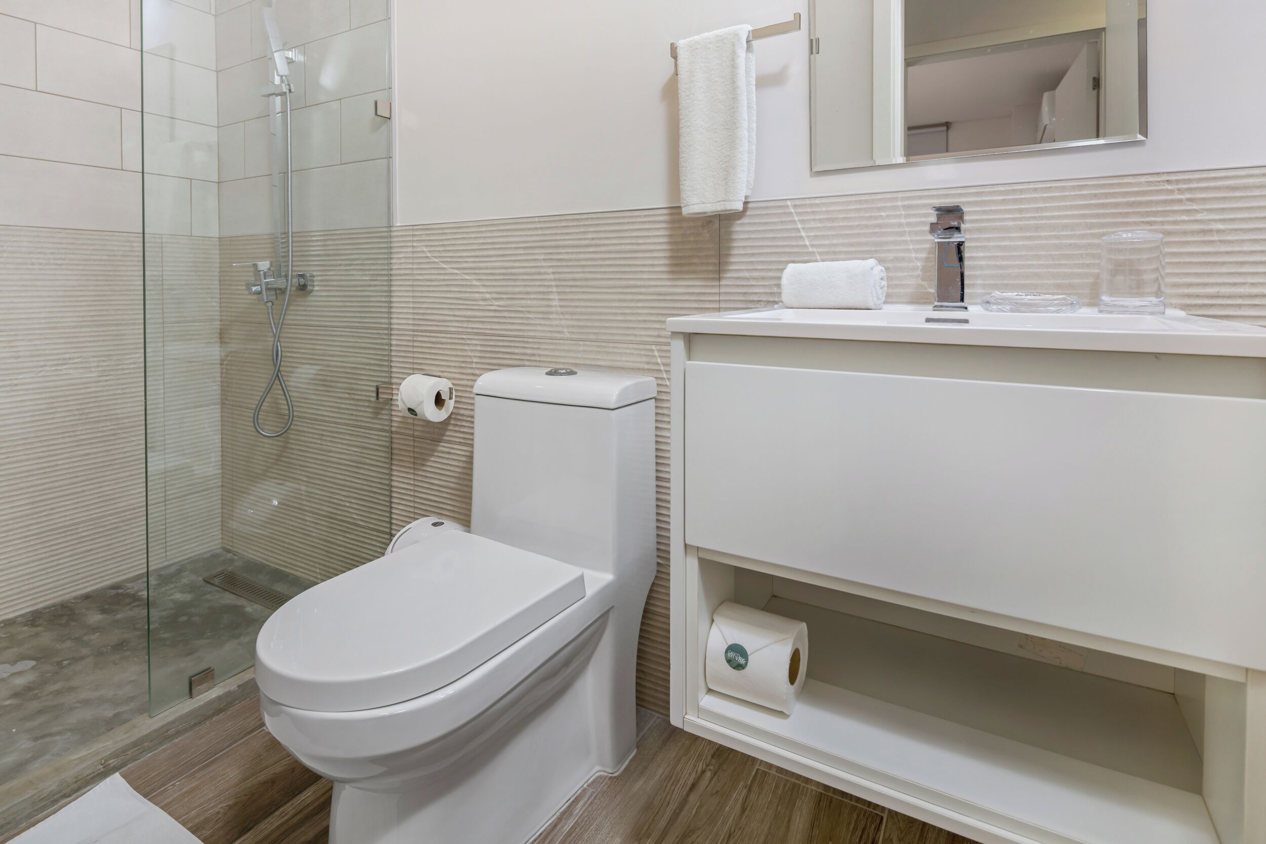 Un baño moderno con ducha envuelta en vidrio, inodoro blanco y tocador con espejo y lavabo.